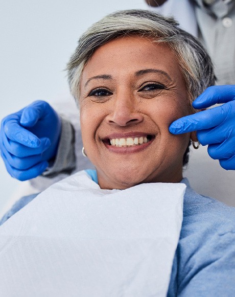 Dentist in blue gloves touching cheek of patient holding mirror and smiling