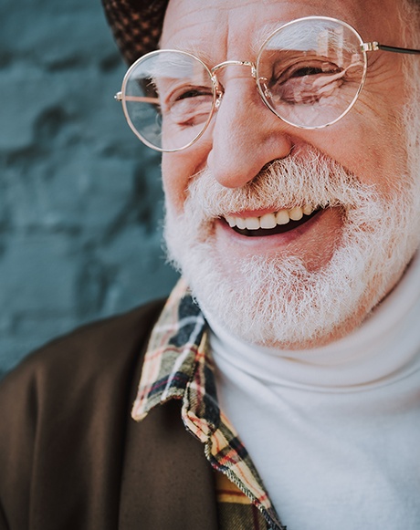 Senior man with glasses smiling in front of brick wall