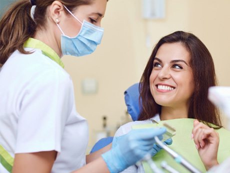 Dentist in white scrubs and blue gloves discussing treatment with a woman with brown hair
