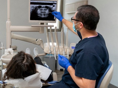 Dentist in blue scrubs and gloves showing a patient her X-rays