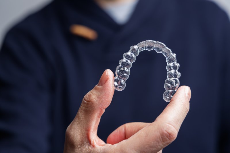 A blurred dentist holding an Invisalign aligner